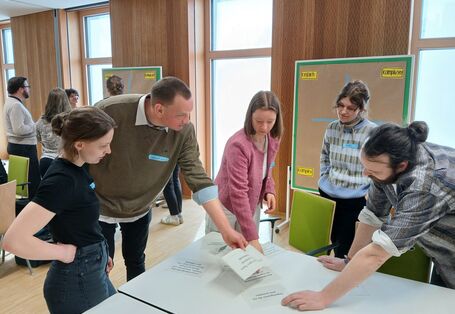 Fünf junge UBA-Wissenschaftler*innen stehen um einen Tisch herum und arbeiten gemeinsam an einer Aufgabe. 
