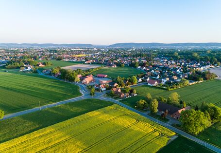 Luftbild einer Siedlung umgeben von Wiesen und Feldern.
