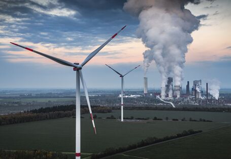 Landschaft mit Windrädern und Kraftwerk, aus dem Rauch aufsteigt