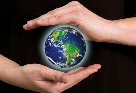 ein Mensch hält seine Hände schützend um den Planeten Erde