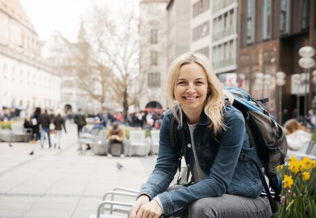 eine Frau sitzt in einer Fußgängerzone und lächelt in die Kamera