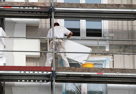 Bauarbeiter auf einem Gerüst bringen Dämmplatten an der Fassade eines Mehrfamilienhauses an.