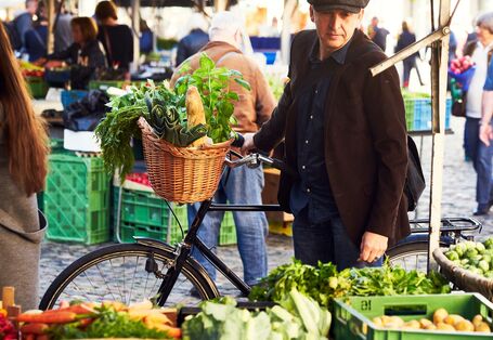 Ein Mann kauft auf einem Wochenmarkt mit seinem Fahrrad Gemüse ein