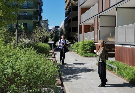 Menschen auf einem Fußweg in einer begrünten mehrgeschossigen Wohnsiedlung mit Balkonen