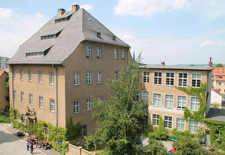 Fassade des Museums im Vordergrund eine Straße, vor dem Gebäude steht eine Gruppe von Menschen