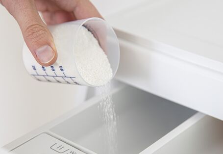 Jemand füllt Waschpulver in eine Waschmaschine.