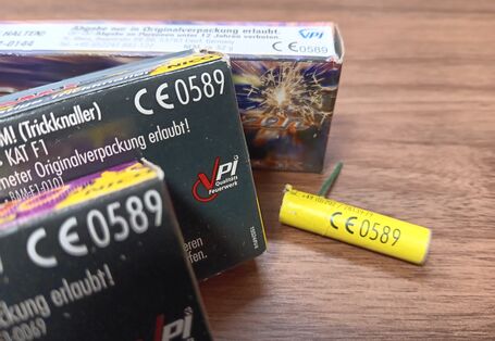 Nahaufnahme von Feuerwerkskörpern mit deutlich sichtbarer CE 0589-Kennzeichnung auf der Verpackung und einer gelben Knallpatrone, die die Konformität mit EU-Sicherheitsstandards belegt.