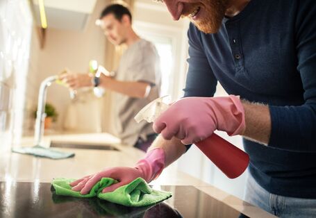 Ein Mann im Vordergrund reinigt das Kochfeld, ein Mann im Hintergrund reinigt den Wasserhahn.