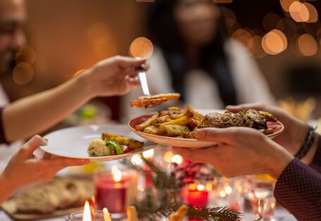 Eine Person serviert einer anderen Person gegartes Gemüse auf den Teller. Es herrscht ein weihnachtliches Ambiente.