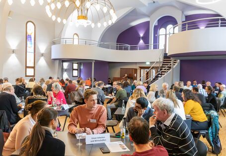 Das Foto zeigt Bürger*innen, die an Gruppentischen diskutieren in einer Beteiligungsveranstaltung zur Deutschen Anpassungsstrategie.