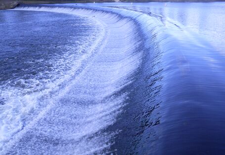 Foto: Ein von Wasser überflossenes, sichelförmiges Wehr.