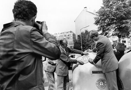 Eigenhändig beklebt der erste Präsident des Umweltbundesamtes, Heinrich Freiherr von Lersner (2. v. l.), einen Altglascontainer mit dem Umweltzeichen. 