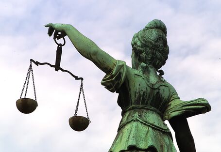 Eine Frauenstatue hält in ihrer linken Hand eine Waage, welche sie mit ausgestrecktem Arm präsentiert.