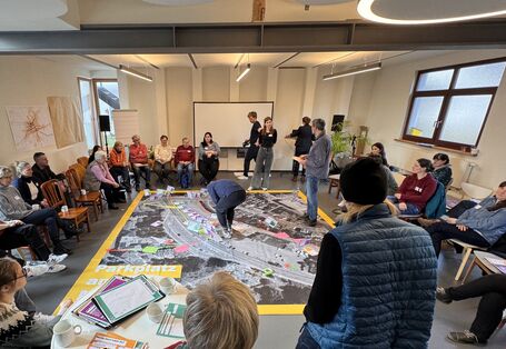 Bürger*innen stehen um eine große Karte auf dem Boden herum und markieren dort Stellen, die bereits gut sind, schlecht sind und Ideen was besser gemacht werden könnte. Hier bei geht es insbesondere um das Thema Mobilität.