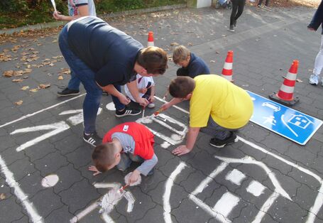 Eltern und Kinder malen das Straßenschild "verkehrsberuhigter Bereich" auf den Asphalt