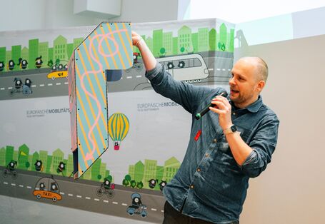 Ein Mann hält ein für die EMW erstelltes umgedrehtes Periskop hoch, mit dem es möglich sein soll die Perspektive von Kindern im Straßenverkehr einzunehmen. 