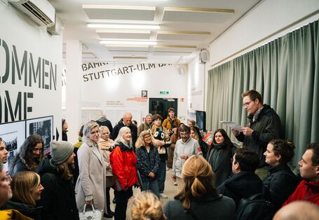 Teilnehmer*innen lauschen dem Vortrag zu den Baumaßnahmen rund um Stuttgart 21. Sie stehen im Ausstellungsraum