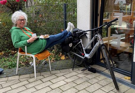 Dame sitzt mit einem Kaffee vor einem Café und lädt den Akku ihres E-Bikes