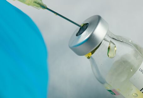 Foto einer Arzneimittelflasche an der eine Spritze aufgezogen wird.