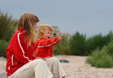 Am Strand sitzen zwei Kinder mit Regenjacken