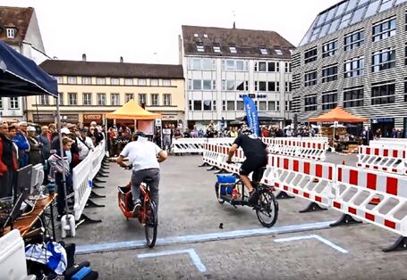 Zwei Lastenradfahrende treten auf dem Marktplatz in Würzburg gegeneinander an. Absperrung ist zu sehen. 