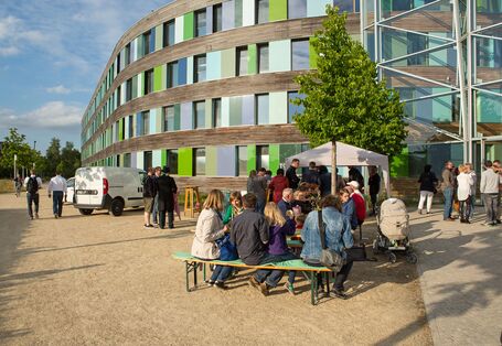 essende Menschen an Biertischen mit Bierbänken vor dem UBA Dessau-Roßlau, an einem weißen Zeltling stehen Menschen an