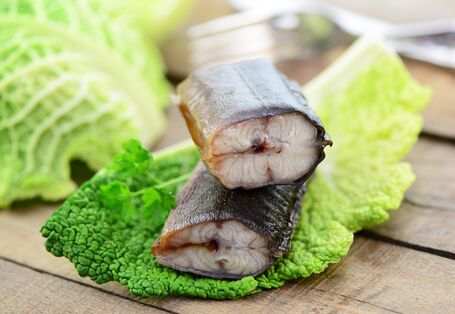 Zwei Stücken Aal auf einem Wirsingkohlblatt liegen auf einem Holztisch, im Hintergrund Messer und Gabel
