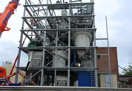 Anlage aus einem mehrstöckigen Metallgerüst mit Bottichen und Rohrleitungen, daneben ein Kran