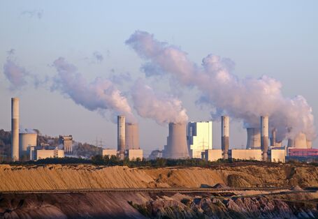 rauchende Schornsteine eines Braunkohlekraftwerks, davor ein Tagebau