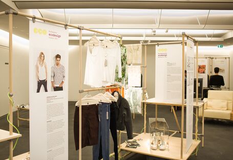 Ausstellung mit Plakaten, die an Holzstangen angebracht sind, und Exponaten wie Kleidung und Schuhen