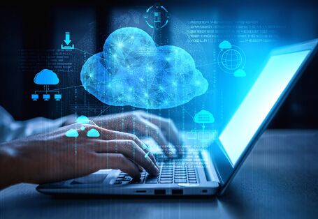 jemand tippt auf einem Laptop, darüber Symbole für Cloud Computing wie Wolken und Download-Pfeil