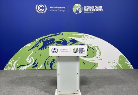 Rednerpult mit der Aufschrift "UN Climate Change Conference UK 2021", im Hintergrund eine Aufstellwand mit derselben Aufschrift und einer Erdkugel