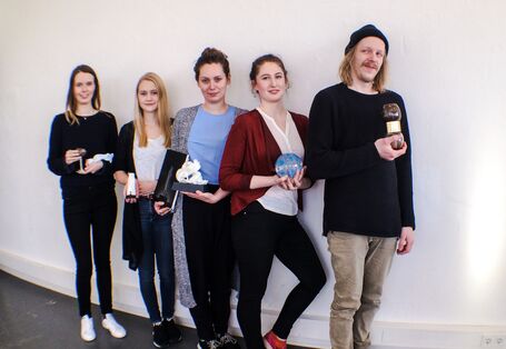 vier junge Frauen und ein junger Mann mit Trophäen in der Hand an eine Wand gelehnt