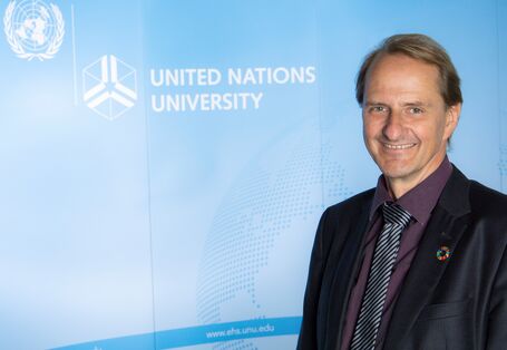 Dirk Messner vor einem blauen Aufsteller mit der Aufschrift "United Nations University" und dem Logo der Vereinten Nationen