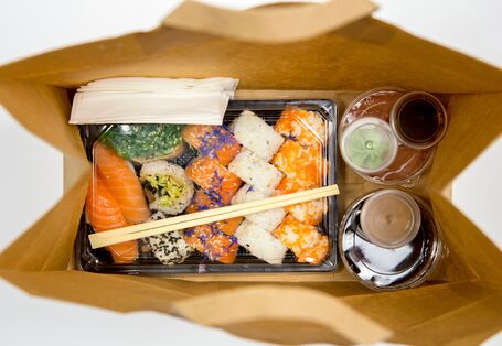 Sushi und mehrere Soßen alle einzeln in Einwegplastikbehältnissen verpackt in einer Papiertüte zum Mitnehmen