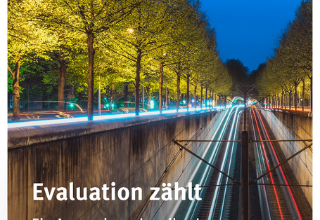 Cover der Broschüre "Evaluation zählt: Ein Anwendungshandbuch für die kommunale Verkehrsplanung" mit einem Foto von einer abgesenkten und beleuchteten Straßenbahntrasse in der Stadt bei Nacht. Unten das Logo "Umweltbundesamt"