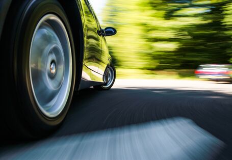ein Auto fährt über eine Fahrbahn, man sieht den rechten Hinterreifen in Großaufnahme