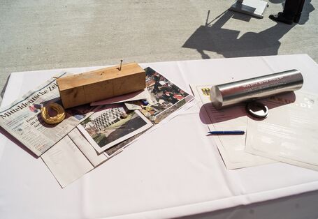 auf einem Tisch liegen eine Metallkapsel, eine Tageszeitung, Geldmünzen, Urkunden, Bauunterlagen und weitere Dokumente