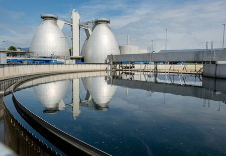 zwei Faultürme einer Kläranlage spiegeln sich in einem Nachklärbecken.