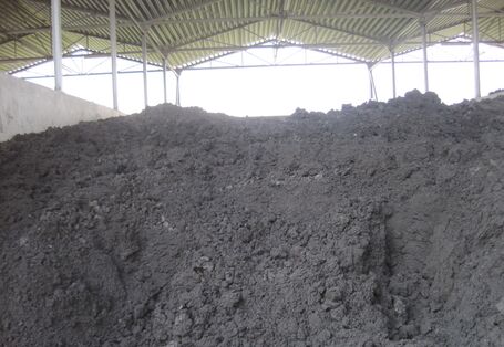 erdartige, dunkelgraue Masse türmt sich in einem überdachten Lagerplatz