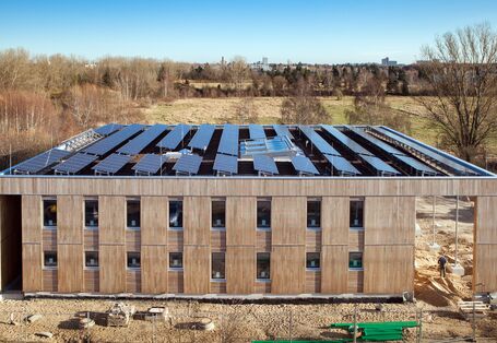 Two-storey square building with wooden façade and solar panels on the roof