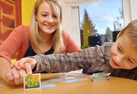 Mutter und Kind beim Memory-Spielen, die Mutter deckt ein Kärtchen mit einer Schlange auf, der Junge schaut neugierig unter die Karte, bevor sie ganz aufgedeckt ist