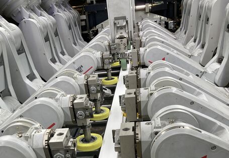 technische Anlage mit 12 Roboterarmen, die eine Folie auf ein PVC-Profil aufbringen