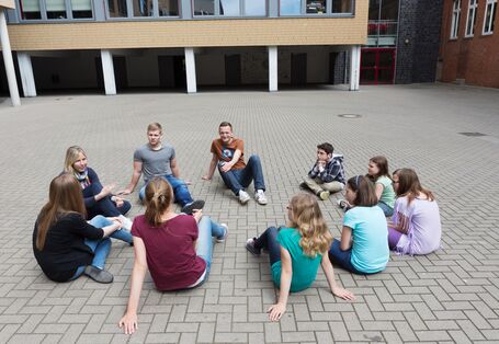 Schüler sitzen im Schulhof, der komplett mit grauen Betonsteinen zugepflastert ist