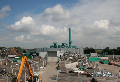 Betriebsanlage mit Metallschrott, auf der Bagger arbeiten, im Hintergrund eine Schredderanlage