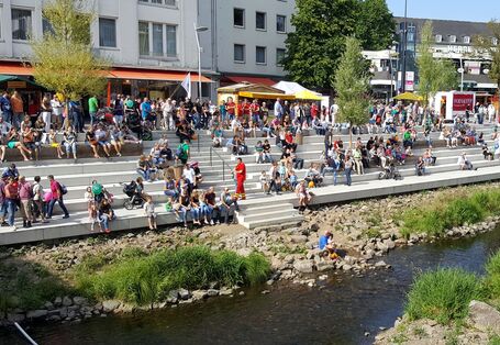 Menschen sitzen auf einer breiten Stufenanlage an einem kleinen Fluss