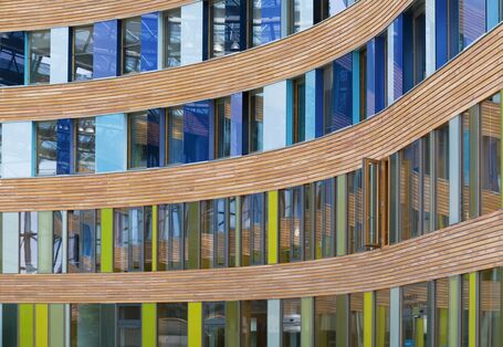 Façade with windows, wood planking and coloured glass slabs in shades of blue and green