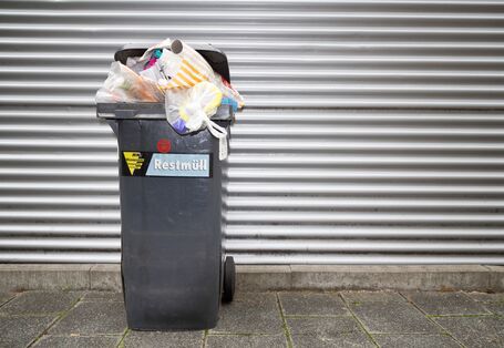 überquellende Restmülltonne auf einem Gehweg