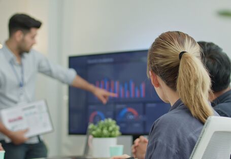 mehrere Personen schauen sich Diagramme auf einem großen Monitor an
