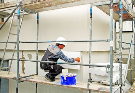 ein Bauarbeiter auf einem Gerüst bringt Dämmplatten aus Polystyrol an einer Hausfassade an